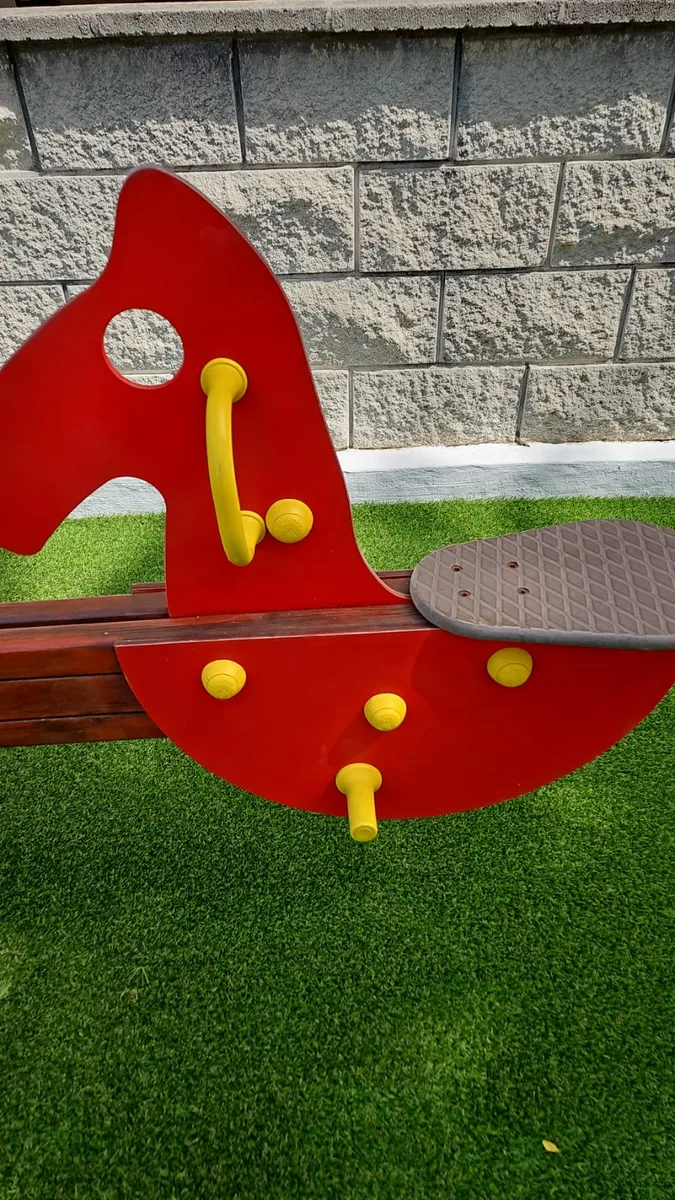 Balancín restaurado y repintado sobre césped artificial en un parque infantil de Dénia