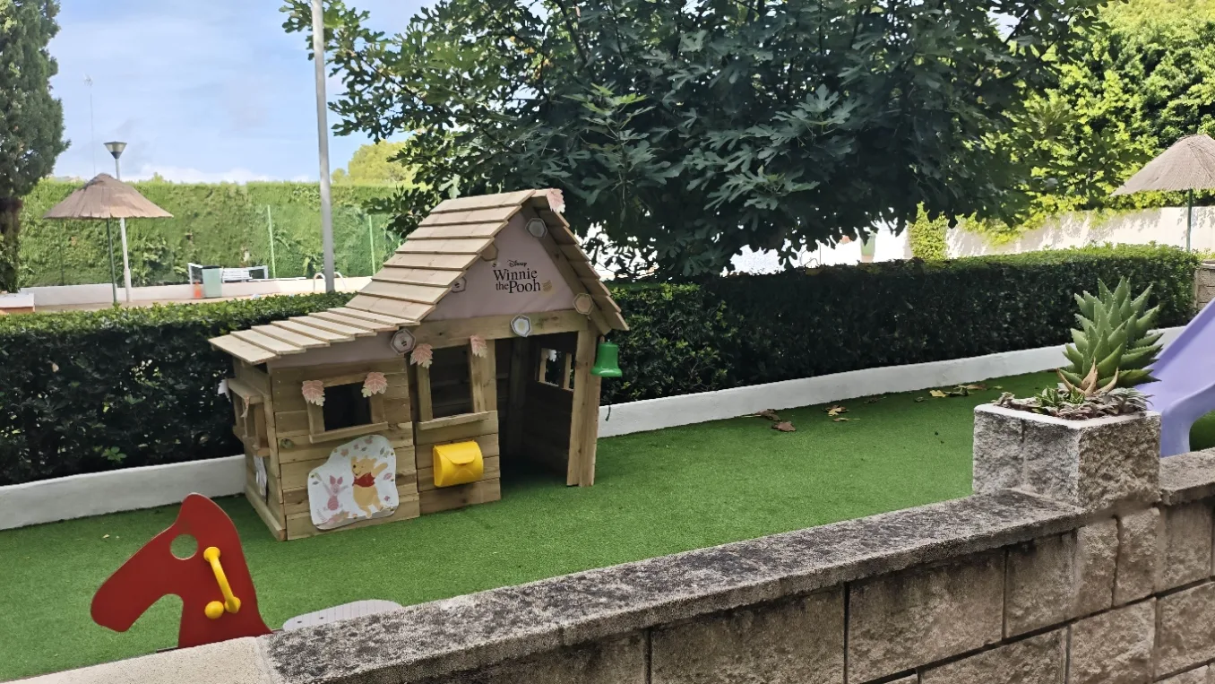 Casita de madera sobre césped artificial en la zona de juegos de una urbanización de Dénia